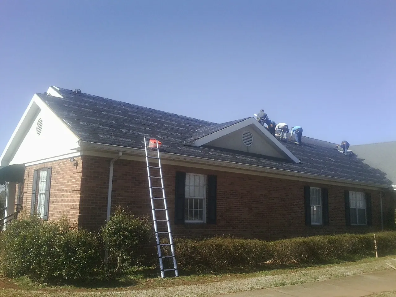 Crew tearing shingles off a brick ranch roof with a ladder set — Emergency Roof Repair work by our crew in Morrisville