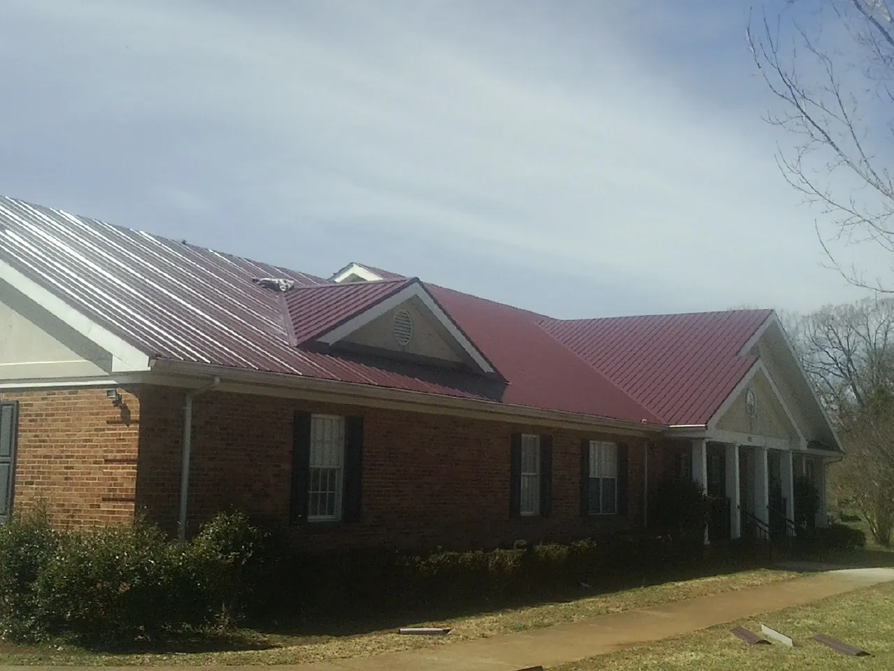 Red metal roof with gabled entries on a long brick building, from a Hail Damage Roof Repair job in Morrisville
