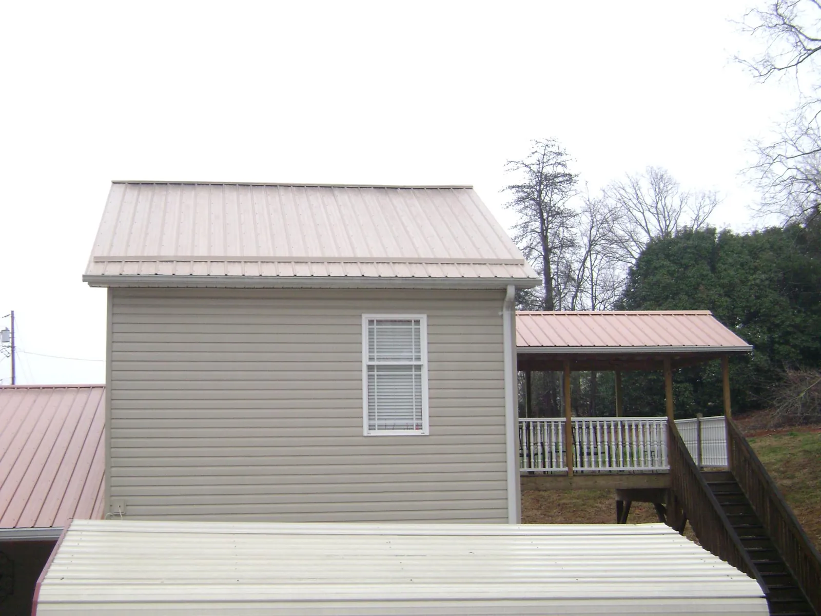 Tan metal roofs on a two story addition and attached porch, from a Roof Replacement job in Morrisville
